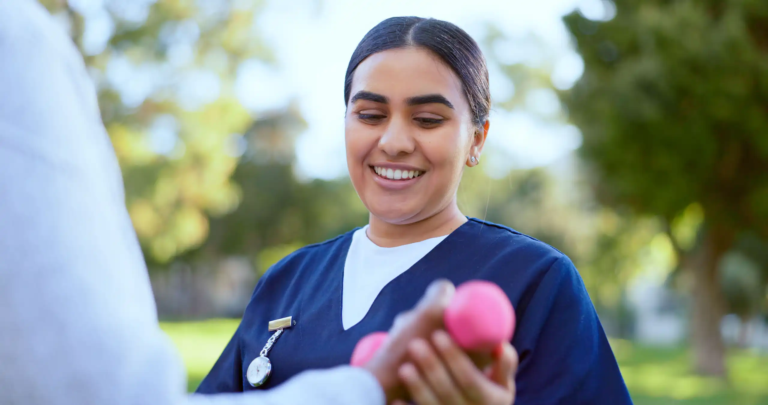A healthcare worker holding a pink exercise weight outdoors, illustrating community nursing.